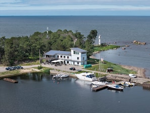 A waterfront property with a large building, docked boats, and a lighthouse in the background. - Vergi Sadam & Restoran Wirkes' (Vergi)