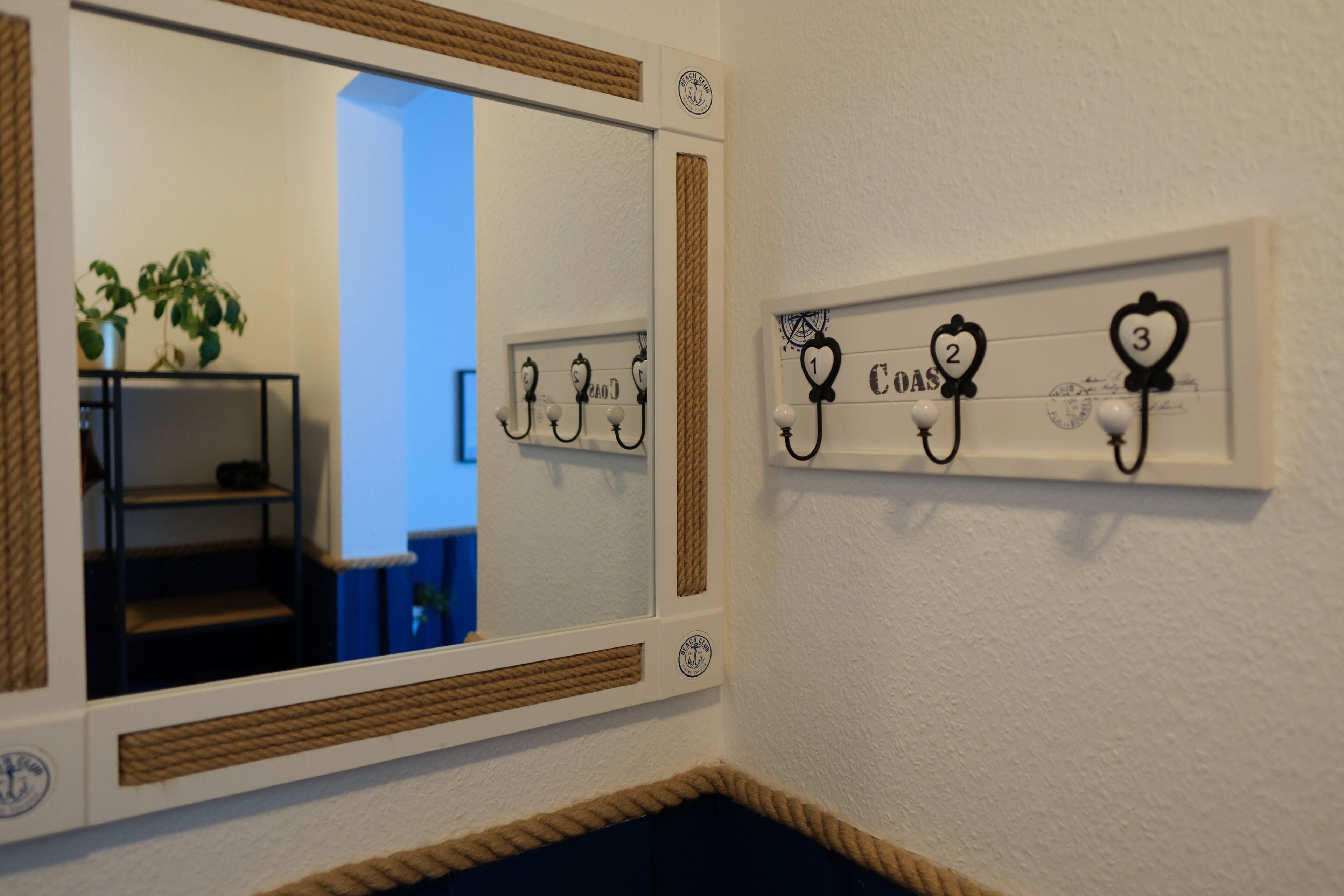 A corner of a room with a large mirror, a coat rack with numbered hooks, and a plant on a shelf.