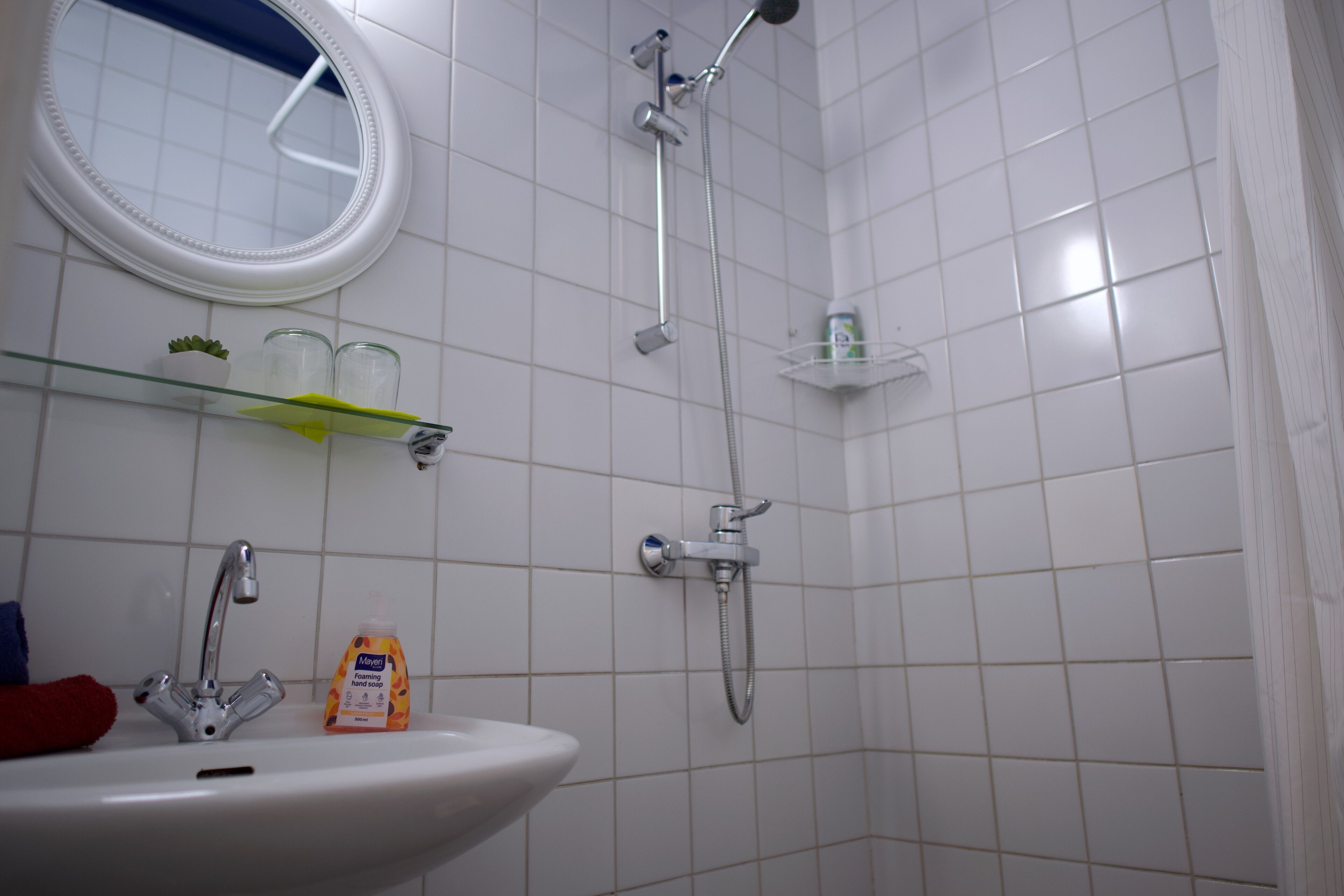 A bathroom with a sink, mirror, shower, and glass shelves.