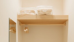 Une salle de bain minimaliste avec un meuble-lavabo en bois, un miroir et une étagère où sont pliées des serviettes.