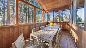 A wooden deck with a table and chairs, large windows, and a view of a forest. - Mountain Majesty: Lake Views, 10-Bedroom, Pool (South Lake Tahoe)