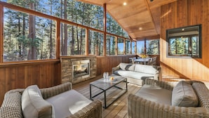 A cozy wooden interior with large windows, a stone fireplace, wicker furniture, and a dining area. - Mountain Majesty: Lake Views, 10-Bedroom, Pool (South Lake Tahoe)