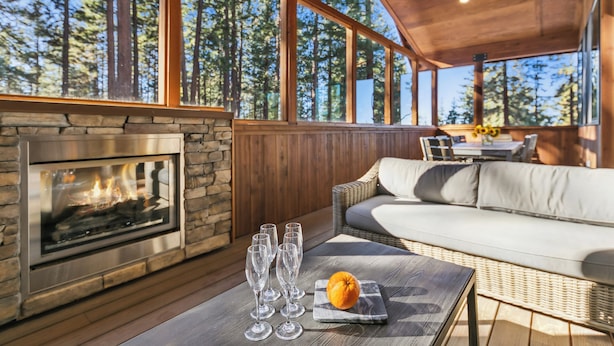 A cozy outdoor seating area with a stone fireplace, wicker furniture, and a view of tall trees. - Mountain Majesty: Lake Views, 10-Bedroom, Pool (South Lake Tahoe)
