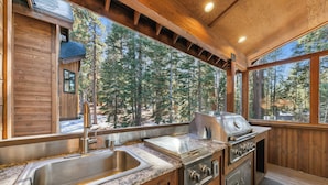 A wooden cabin with a kitchen featuring a sink, stove, and large windows overlooking a forest. - Mountain Majesty: Lake Views, 10-Bedroom, Pool (South Lake Tahoe)