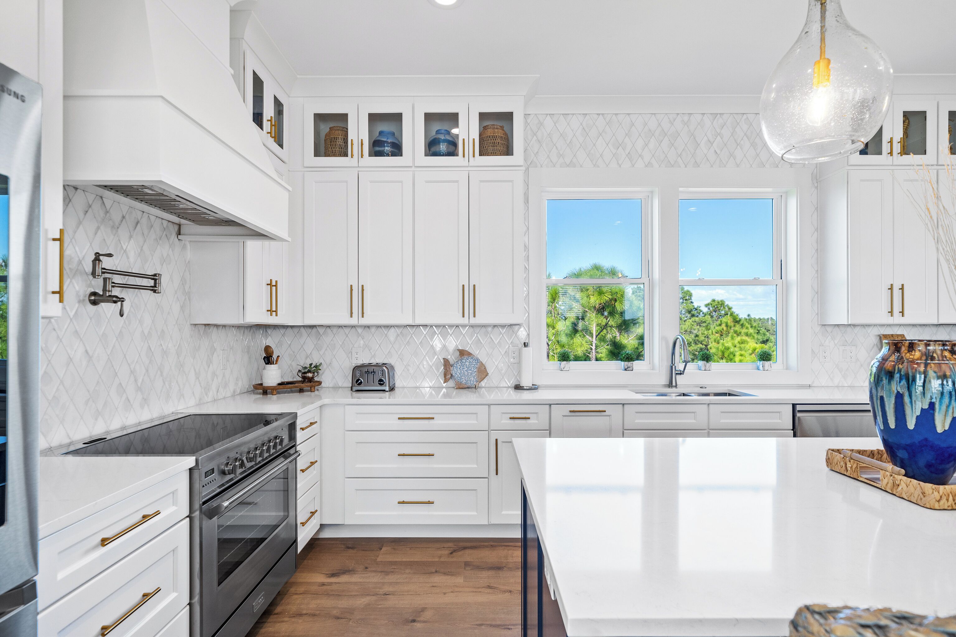 Una cocina moderna con armarios blancos, una isla grande y vistas a la vegetación.