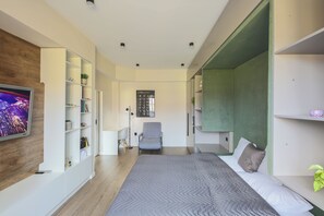 A modern bedroom with a bed, a TV, a desk, and a chair.