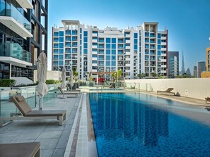 A modern hotel with a rooftop pool, multiple balconies, and a view of the city skyline.