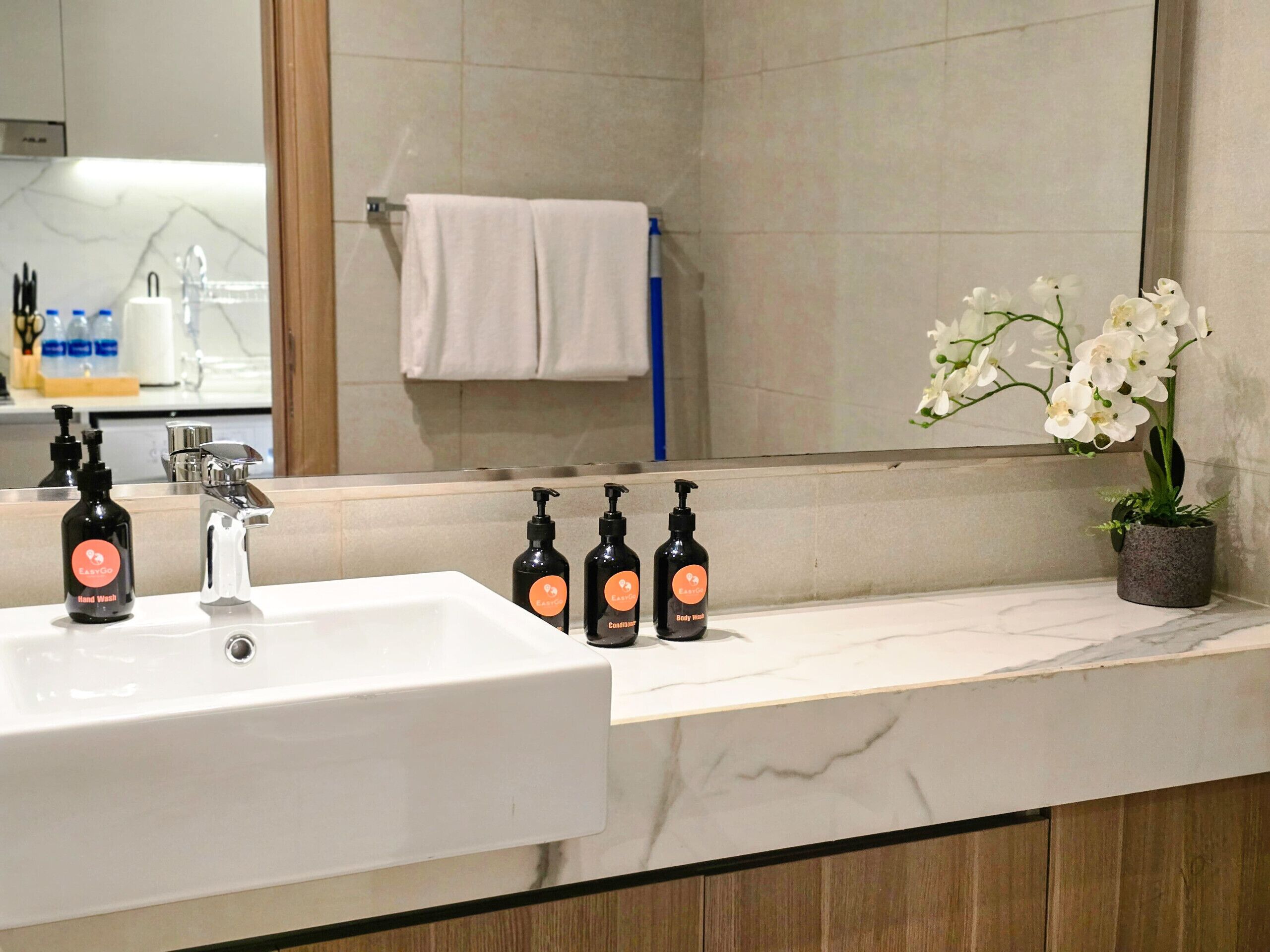 A bathroom with a white sink, three hand wash bottles, a body wash bottle, a potted orchid, and a towel rack.