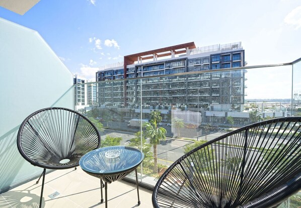 A balcony with two chairs and a small table, overlooking a modern building with multiple floors and a parking area below.
