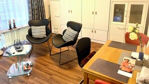 Una sala de estar moderna con comedor, que incluye una mesa de madera, sillas negras, una mesa baja de vidrio y armarios blancos.