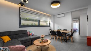 Una sala de estar moderna con un sofá gris, una mesa de centro redonda y un comedor con una mesa y sillas de madera.