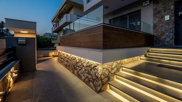 Un edificio moderno con fachada de piedra, una terraza de madera y una escalera que lleva a un nivel superior.