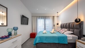 Un dormitorio moderno con una cama grande, una mesita de noche, un aparador, un reposapiés rojo y un televisor en la pared.
