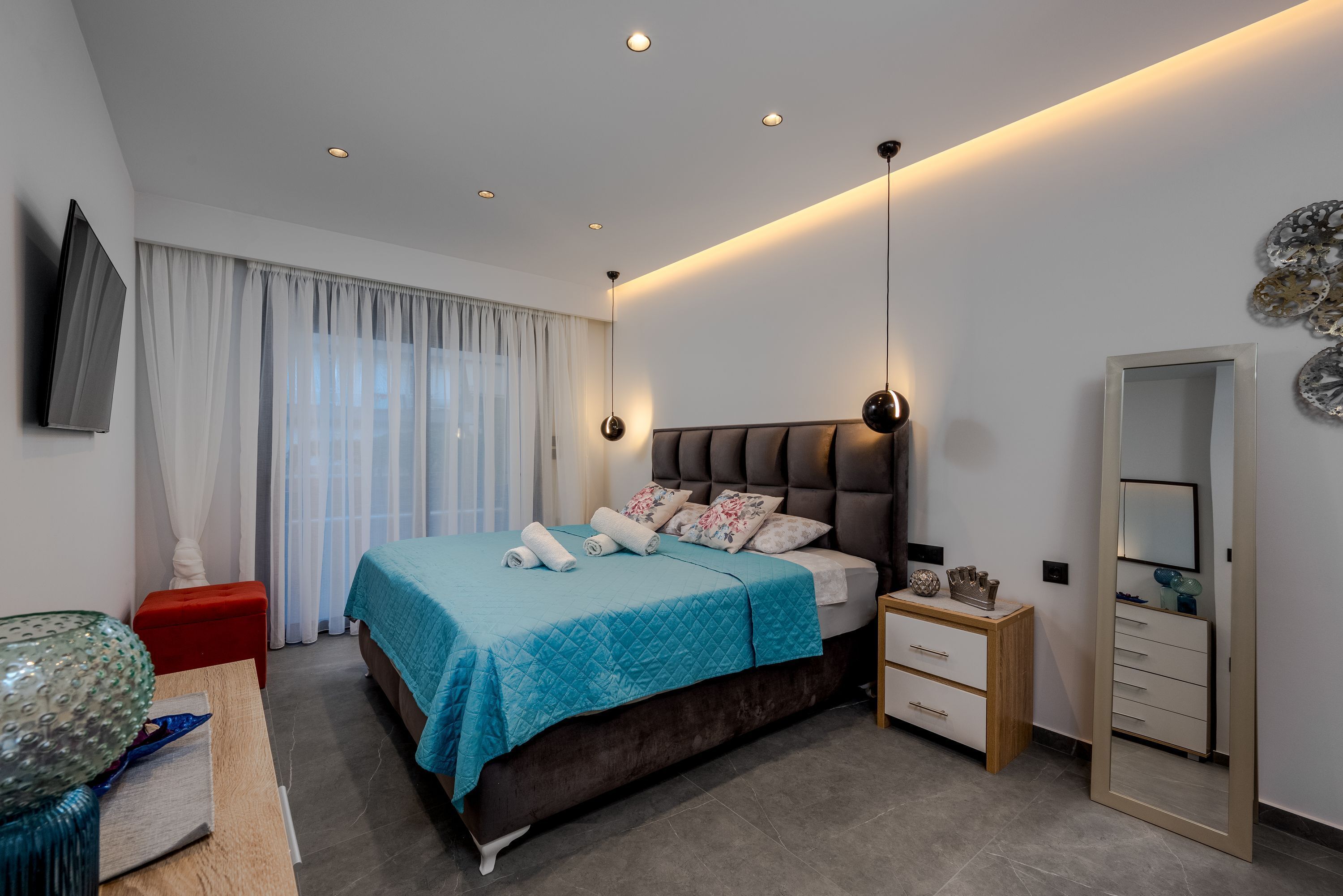 A modern bedroom with a bed, bedside table, dresser, and a large mirror.