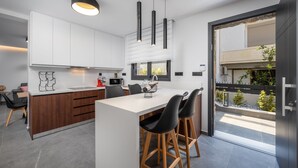 Una cocina moderna con armarios blancos, una isla central con taburetes, iluminación colgante y vistas al exterior.