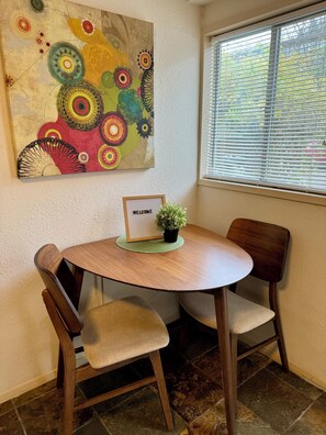 A round wooden table with two chairs, a welcome sign, and a small potted plant.