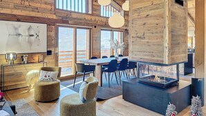 A spacious living area with wooden beams, a large window, a fireplace, and modern furniture. - Chalet Combloran Mont Blanc view (Combloux)