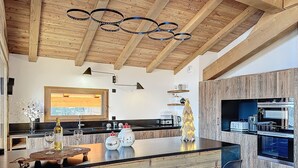 A modern kitchen with a wooden ceiling, a central island with bar stools, and a built-in oven. - Chalet Combloran Mont Blanc view (Combloux)