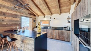 A modern kitchen with wooden beams, a central island with bar stools, and a large oven. - Chalet Combloran Mont Blanc view (Combloux)