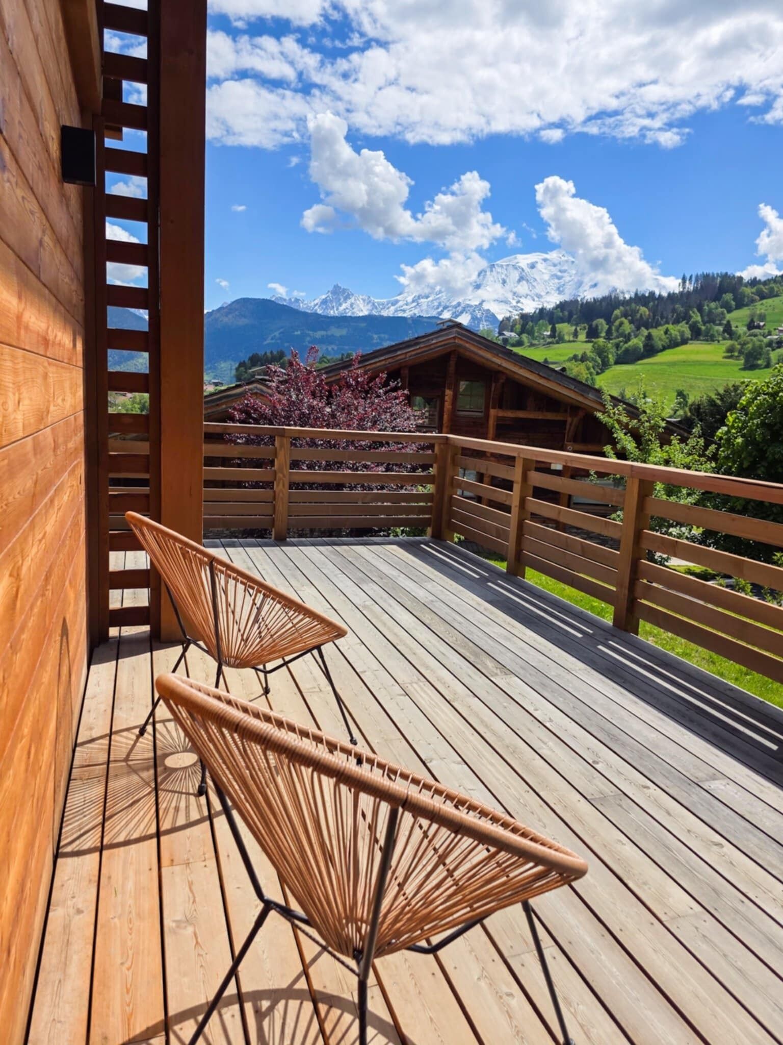 Une terrasse en bois avec deux fauteuils en osier, une balustrade en bois et une vue sur un paysage montagneux.