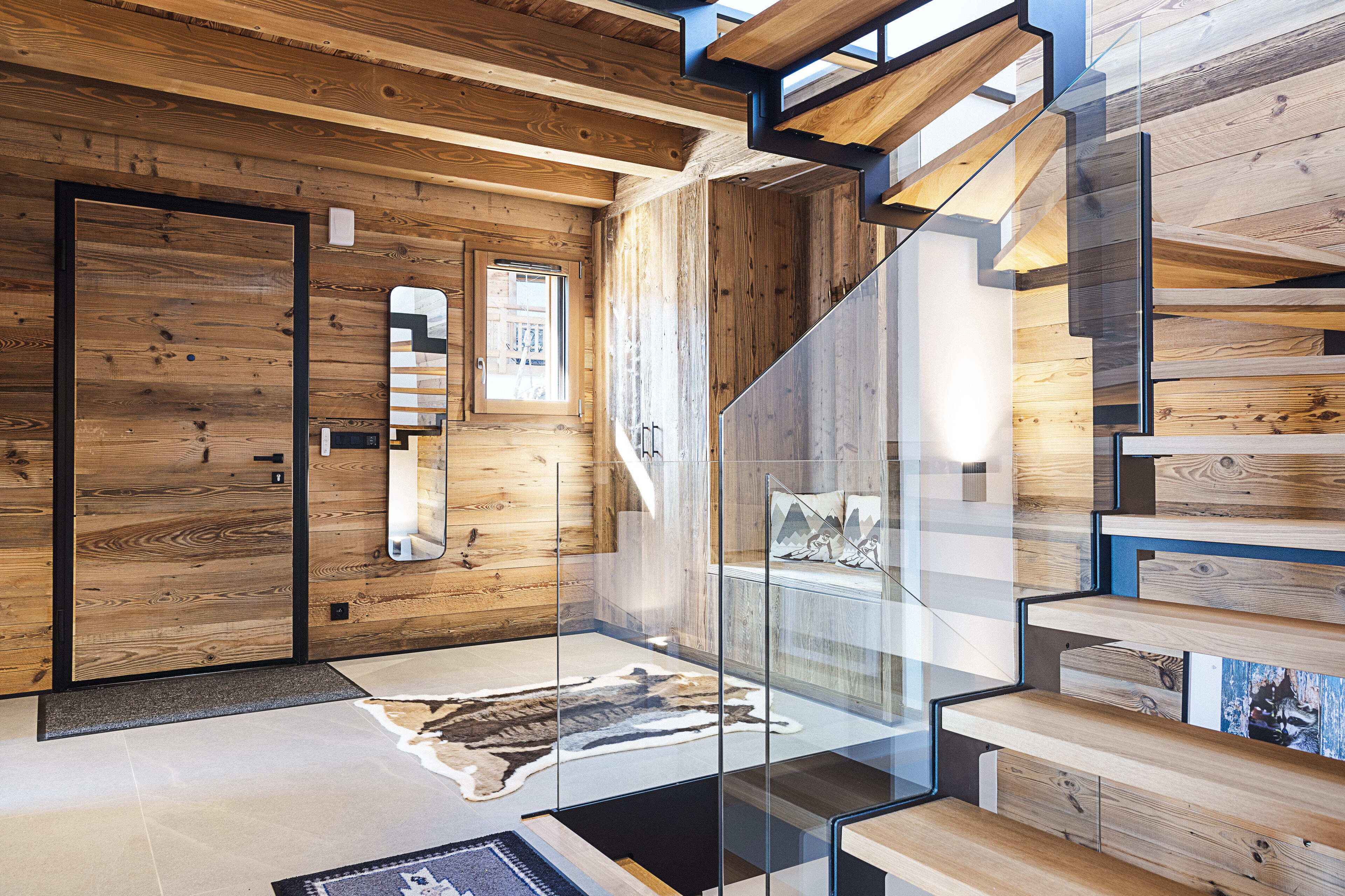 A modern interior with wooden paneling, a glass staircase, and a leather rug.
