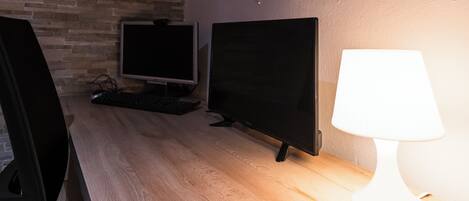 Un escritorio de madera con dos monitores, un teclado y una lámpara de escritorio blanca.
