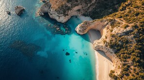 Vista aérea de una zona costera con aguas turquesas cristalinas, acantilados rocosos y una playa estrecha.