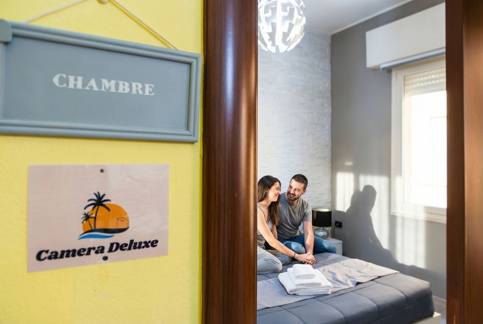 Een kamer met een bed, een bord aan de muur waarop 'CHAMBRE' staat en een poster voor 'Camera Deluxe'.