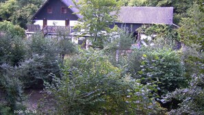 Een huis omringd door weelderige begroeiing, met een zichtbaar balkon en een rode deur.