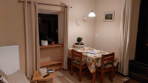 Een gezellige woonkamer met een bank, een klein tafeltje met een afstandsbediening, een eettafel met stoelen en een potplant.