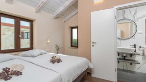 A bedroom with a bed, a bedside table, a window, a door, and a bathroom with a sink and mirror.