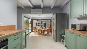 A modern kitchen with green cabinets, a stainless steel refrigerator, and a dining area with wooden chairs.