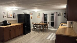 Uma cozinha compacta com geladeira preta, armários de madeira, uma mesa de jantar com cadeiras e uma janela com cortinas.