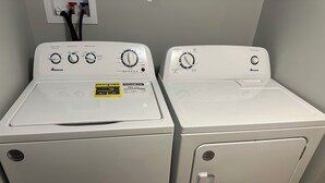 Duas máquinas de lavar roupa Amana brancas de abertura frontal, com painéis de controlo, etiquetas ENERGY GUIDE e uma tomada elétrica na parede com uma ficha de três pinos.