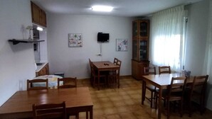 A dining area with wooden tables and chairs, a television on the wall, and a cabinet with glass doors.
