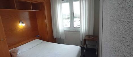 Un dormitorio pequeño y ordenado con una cama individual, un armario de madera, una mesita y un televisor montado en la pared.