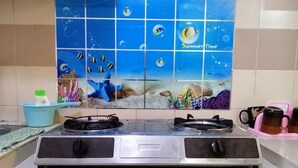 Una cocina con estufa a gas, salpicadero de azulejos que representa una escena submarina y un portavasos rosa.