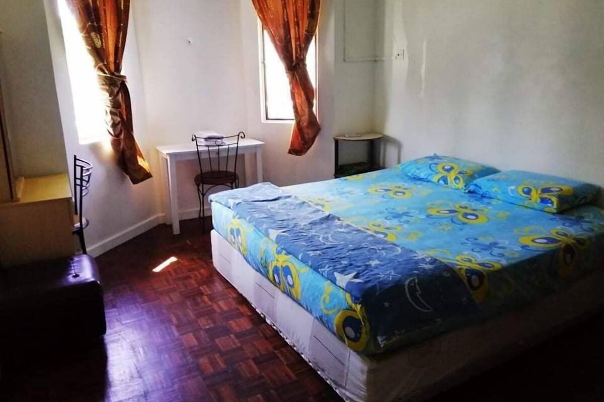 A bedroom with a bed, a desk, and two windows with curtains.