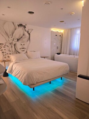 A modern bedroom with a large bed, a wall mural, a small round table, and a bathtub. - UP Hotel Boutique (Bombinhas)