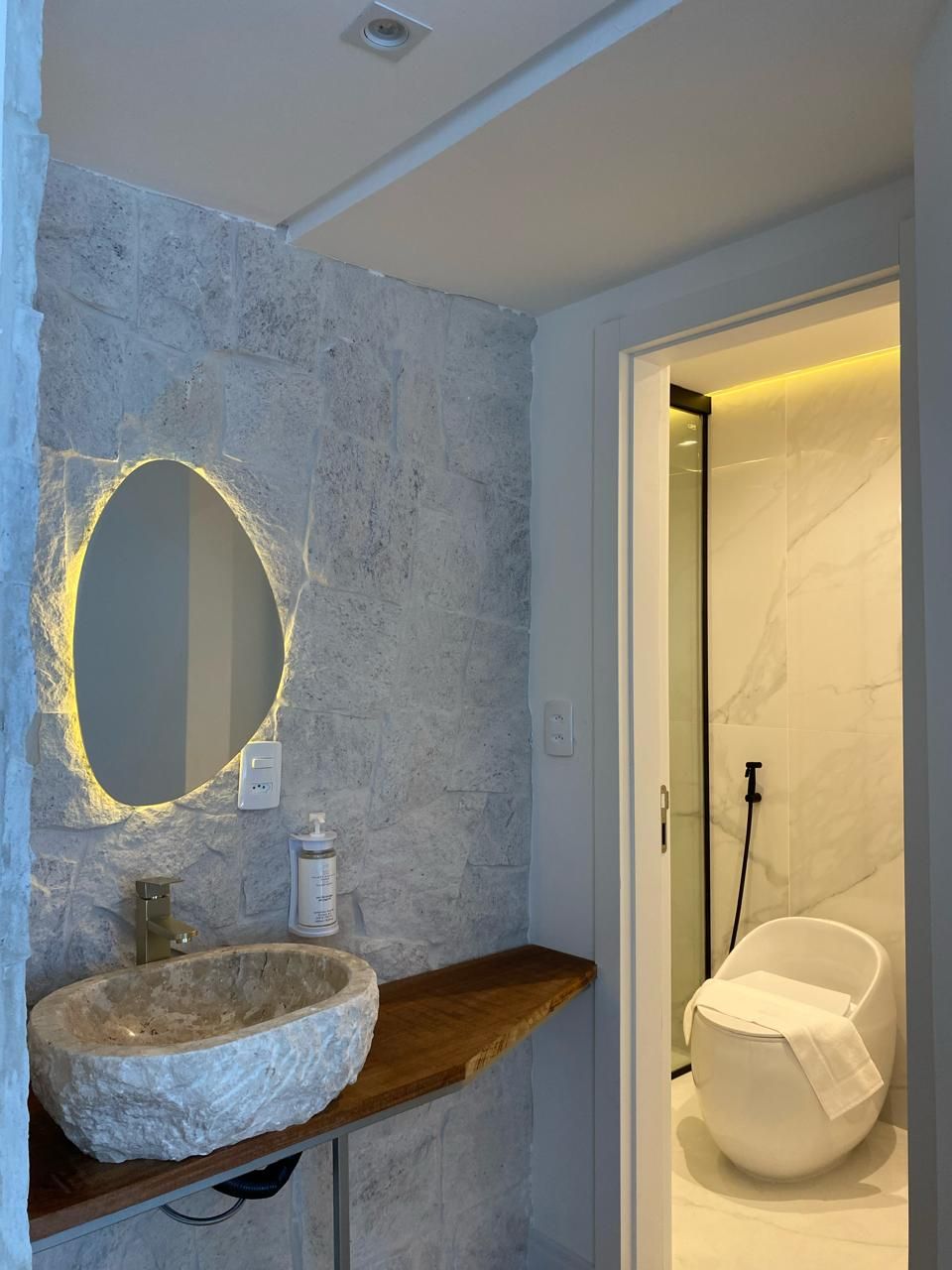 Une salle de bain avec un lavabo en pierre, un miroir rond et des toilettes modernes.
