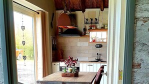 Une cuisine rustique avec un mur recouvert de briques, des poutres en bois au plafond et un coin repas comprenant une table et des chaises.