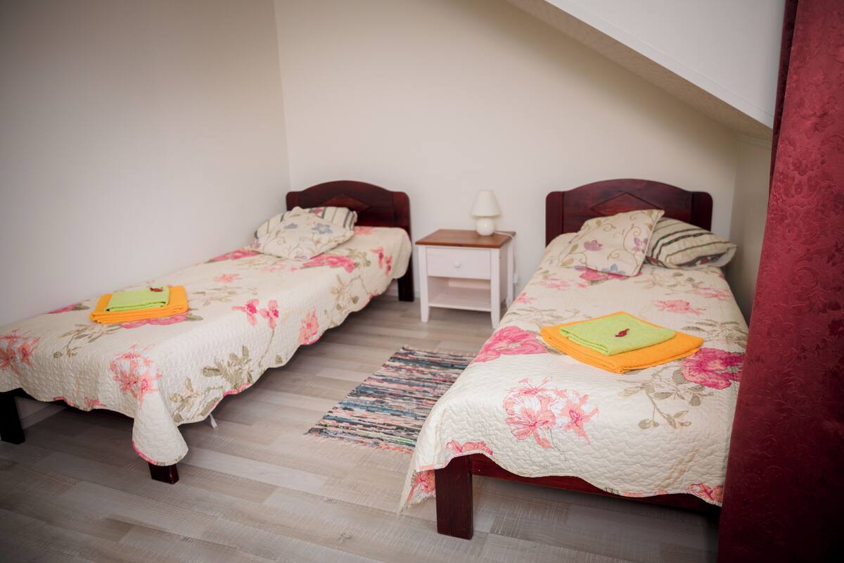 A bedroom with two single beds, a nightstand, and a lamp.