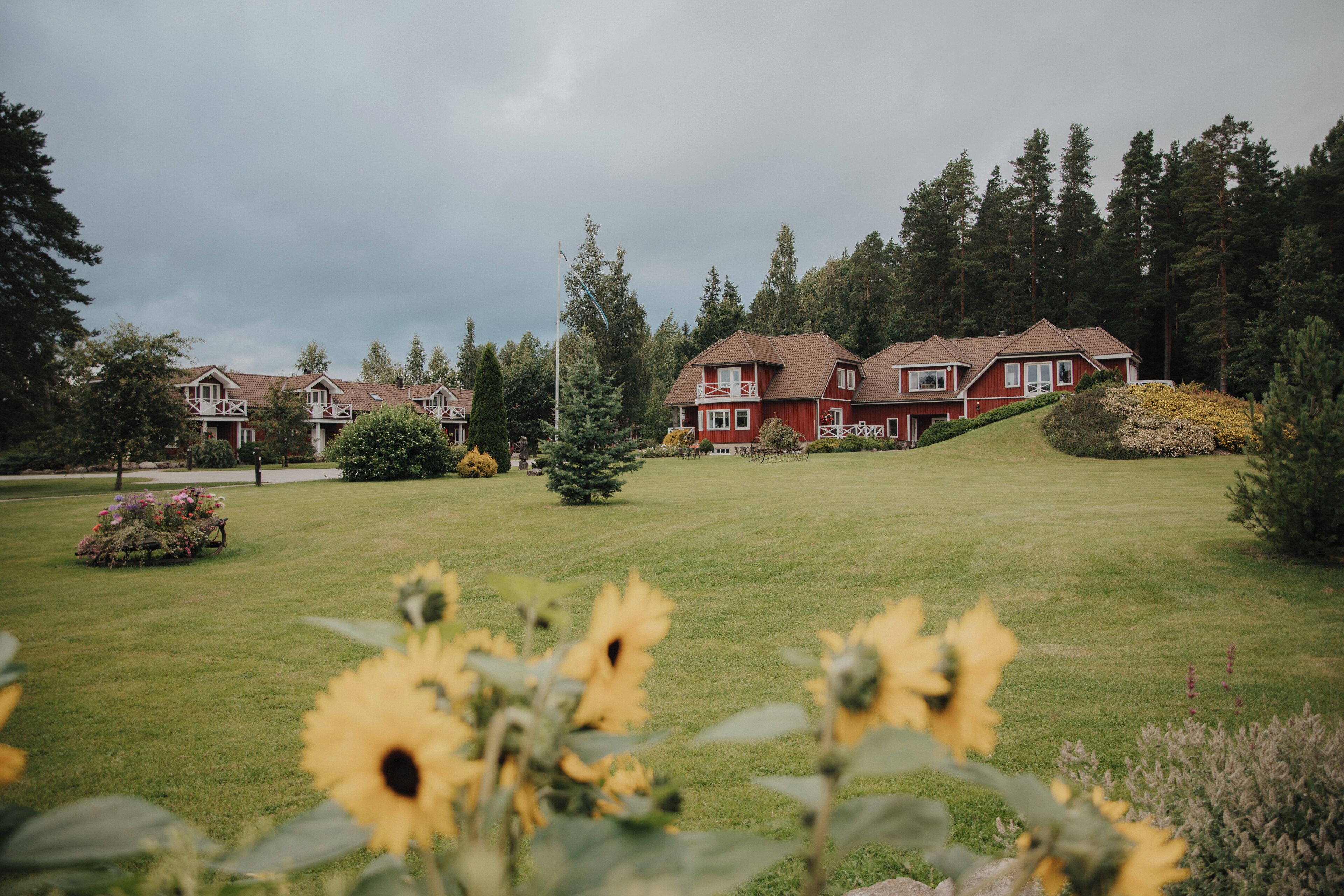 A large red building with multiple windows and a sloped roof, surrounded by a well-maintained lawn and trees.