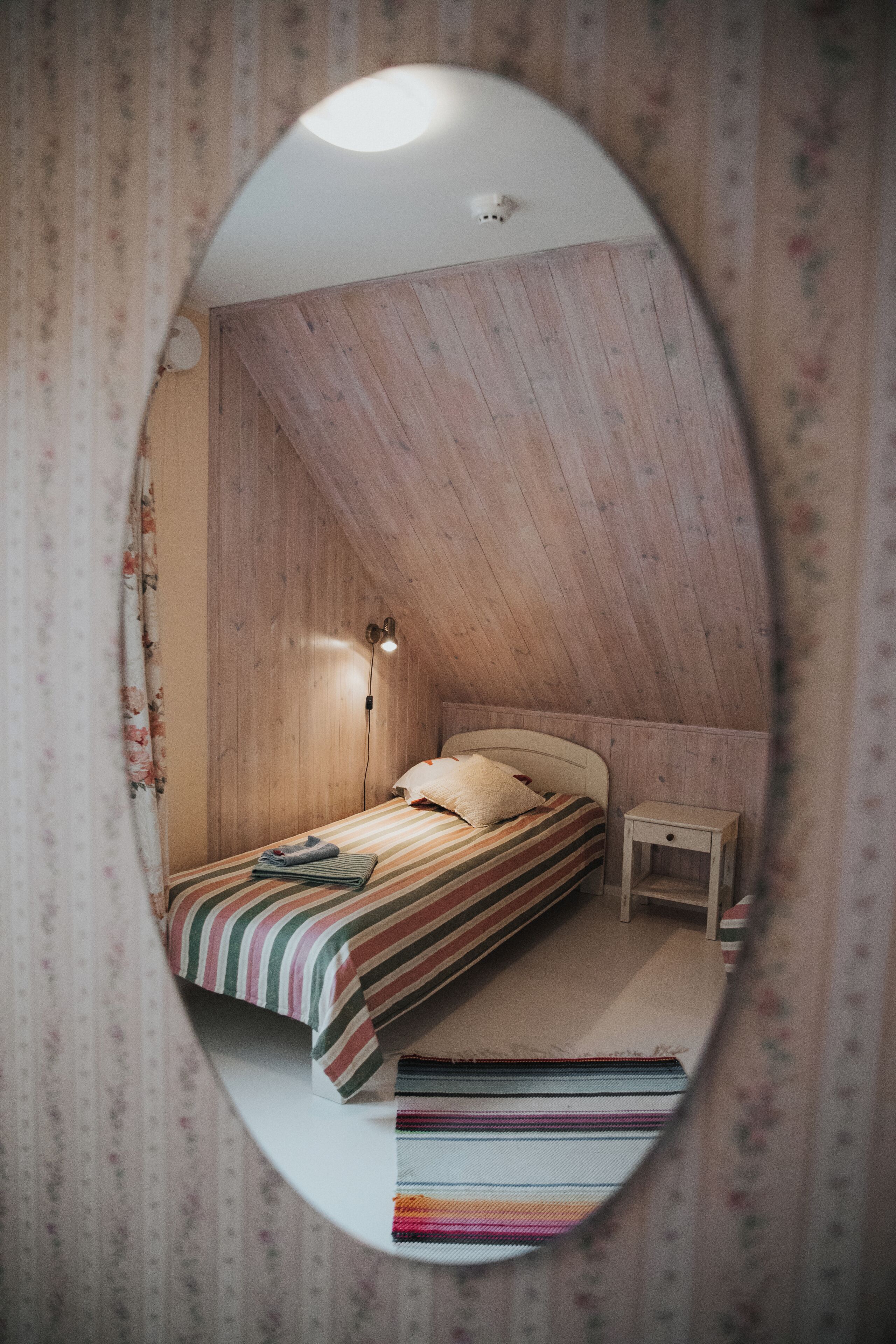 Un dormitorio con techo inclinado de madera, una cama individual con ropa de cama a rayas, una mesita de noche y una pequeña alfombra.