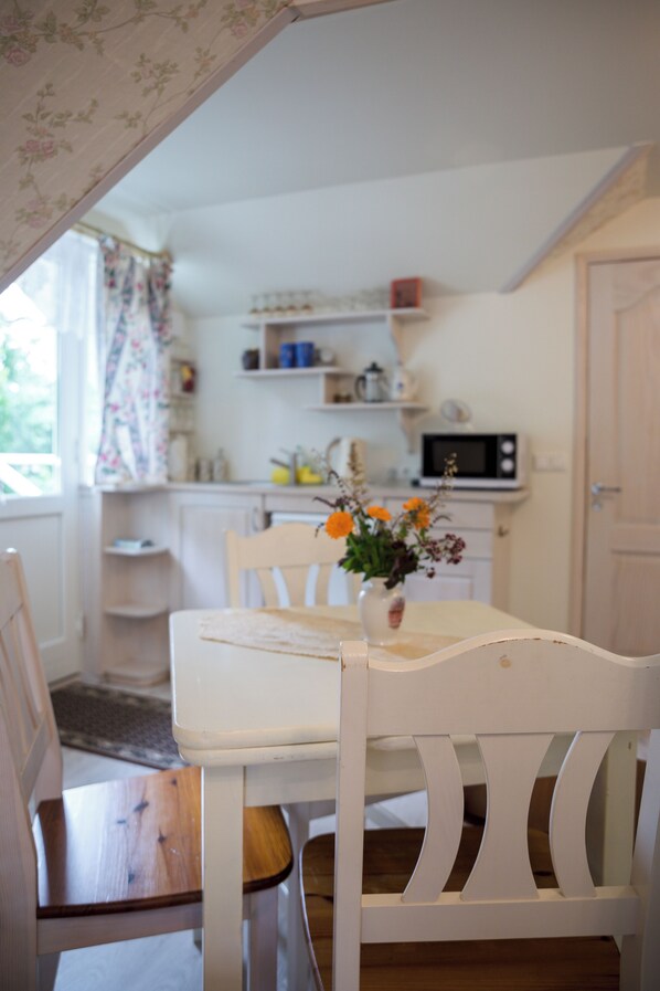 A dining area with a white table and chairs, a vase with flowers, and a kitchen in the background. - Klaara-Manni Holiday Center (Randivälja)