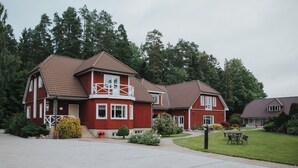 A red two-story house with a balcony, surrounded by a well-maintained lawn and trees. - Klaara-Manni Holiday Center (Randivälja)