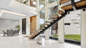 A modern interior with a staircase, a dining area, and large windows. - Gated 9BR Estate for 20 w/ Private Pool, Jacuzzi, Theater & Guest House! Pet-Friendly! (Southwest Ranches)