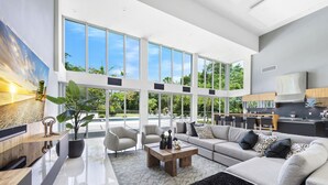 A spacious living area with a large window overlooking a pool, a modern kitchen, and a seating area with a sofa and chairs. - Gated 9BR Estate for 20 w/ Private Pool, Jacuzzi, Theater & Guest House! Pet-Friendly! (Southwest Ranches)