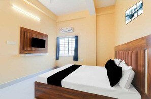 A hotel room with a bed, a mounted TV, a window with curtains, and a wall-mounted air conditioner. - Roomssolution Patna (Patna)