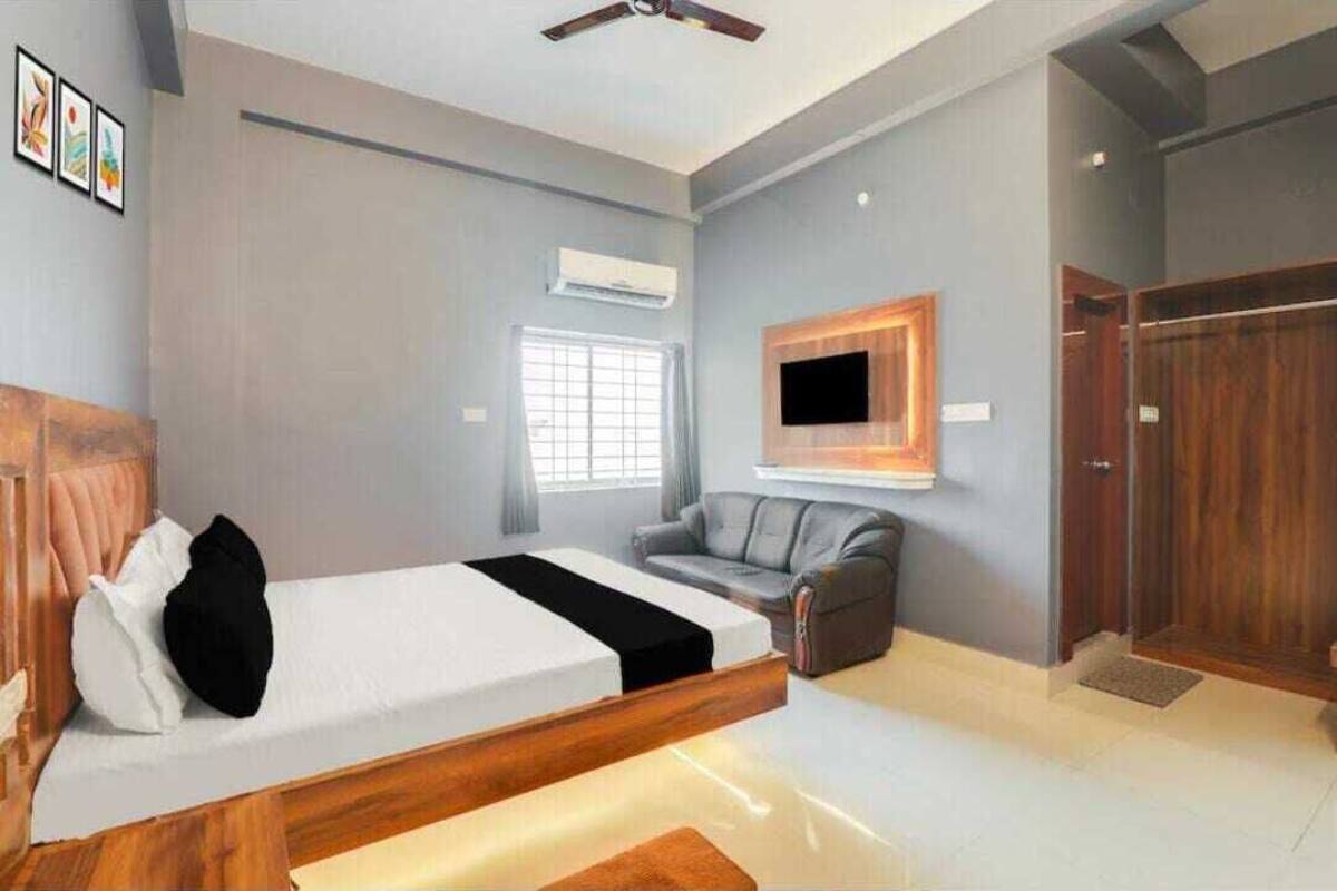 A bedroom with a bed, a gray sofa, a TV mounted on the wall, and a wooden wardrobe.